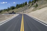 a view down an asphalt roadway at the bottom of a mountain near a house with a truck driving through it