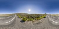 a paved country road runs through the desert with grass and rocks around it and the sun shining on the horizon