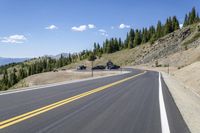 a scenic country road and vehicle stop with mountain view in background with pine trees on hillside near parking area