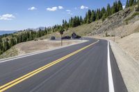 a scenic country road and vehicle stop with mountain view in background with pine trees on hillside near parking area