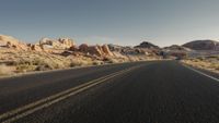 a man rides on the back of a motorcycle down a desert road between rocks and brush