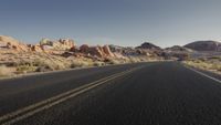 a man rides on the back of a motorcycle down a desert road between rocks and brush