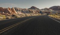 a man rides on the back of a motorcycle down a desert road between rocks and brush