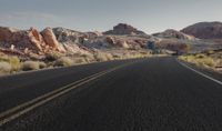 a man rides on the back of a motorcycle down a desert road between rocks and brush