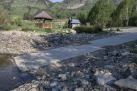 rocks and a path leading to a covered shelter along a riverbank with hills in the background