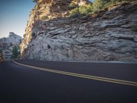 a couple is riding their motorcycle down the road in front of the mountains near a cliff