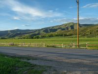 a lone country road is in the countryside area with mountains on both sides and barbed fence between the two sides