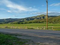 a lone country road is in the countryside area with mountains on both sides and barbed fence between the two sides