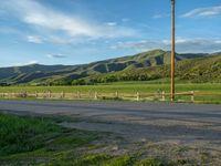 a lone country road is in the countryside area with mountains on both sides and barbed fence between the two sides