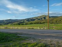 a lone country road is in the countryside area with mountains on both sides and barbed fence between the two sides