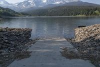 a small dock extending into the water by mountain peaks with a trail to the shore