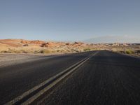 the empty road is lined with desert bushes and sand dunes as the sun sets on the horizon