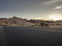 an empty street with a road in the foreground and mountains on the background with the sun