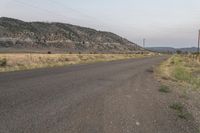 an empty road with powerlines along side of it and mountains in the distance with telephone poles across it