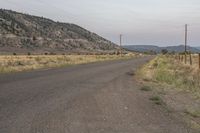 an empty road with powerlines along side of it and mountains in the distance with telephone poles across it