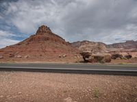 some rocks on the side of the road in front of a mountain range covered in dirt