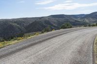 a long dirt road curves into the distance in front of mountains and some bushes and trees