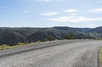 a long dirt road curves into the distance in front of mountains and some bushes and trees