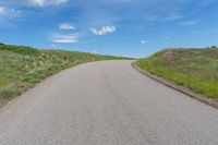 the empty road is surrounded by green grass and blue skies as if for a road trip