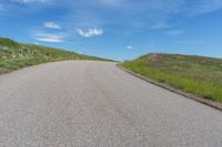 the empty road is surrounded by green grass and blue skies as if for a road trip