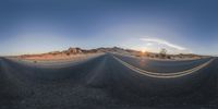 the curved road is empty and paved in a desert setting as the sun sets over a mountain