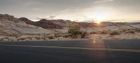 an image of a road in the desert at sunset near some mountains and trees and bushes