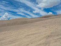 a desert scene with some very big clouds in the sky and some sand dunes with many different colored lines, and the grass has been scattered over allover the tops