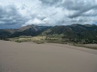 an empty desert landscape surrounded by hills and trees in the distance is a cloud filled sky