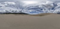 a surreal landscape with clouds over sand dunes and hills in the distance with a person walking