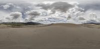 the man rides his snow board in the sand dunes near mountains and clouds behind him