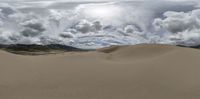 sand dunes in the background with a large white cloud and sun peeking up in the sky