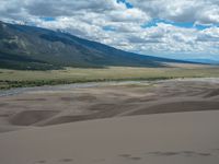 there is a sand hill and some mountains in the distance and a river running in the background