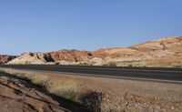 a long paved highway on the side of a cliff covered in sand, shrubs and rocks