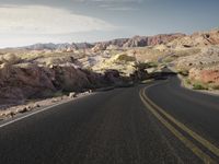 a man walking down a street through the middle of a desert with mountains in the background