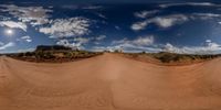 a red dirt road surrounded by clouds and desert on a sunny day with no cars