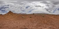 this is an image of a dirt field with desert terrain in the background and the clouds overhead