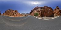 a desert road has a big rock formation with a sun reflecting in the background,