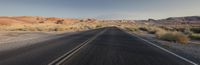 the long empty road near the mountains in the desert is lined with scruby grass