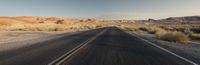 the long empty road near the mountains in the desert is lined with scruby grass