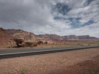 two motorcyclists riding down the road past rock formations on a partly cloudy day