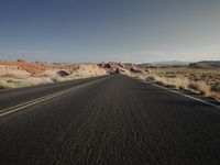 a car is driving down a desert road in the sunlight and mountains are on both sides