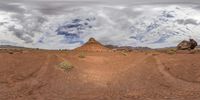 a desert with large rocks near the top of it, under a cloudy sky and clouds