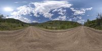 a long dirt road in the middle of nowhere with mountains in the distance below and clouds in the sky