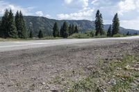 the road is empty and dirt with trees in the background in this image there are rocks and grass