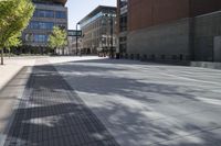 a paved sidewalk in an urban city setting with building in the background and green trees