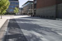 a paved sidewalk in an urban city setting with building in the background and green trees