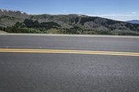 the road is empty but there are yellow lines on it as well as the mountains