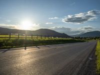 a lone country road is in the countryside area with mountains on both sides and barbed fence between the two sides