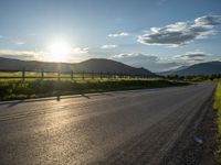 a lone country road is in the countryside area with mountains on both sides and barbed fence between the two sides