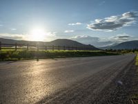 a lone country road is in the countryside area with mountains on both sides and barbed fence between the two sides